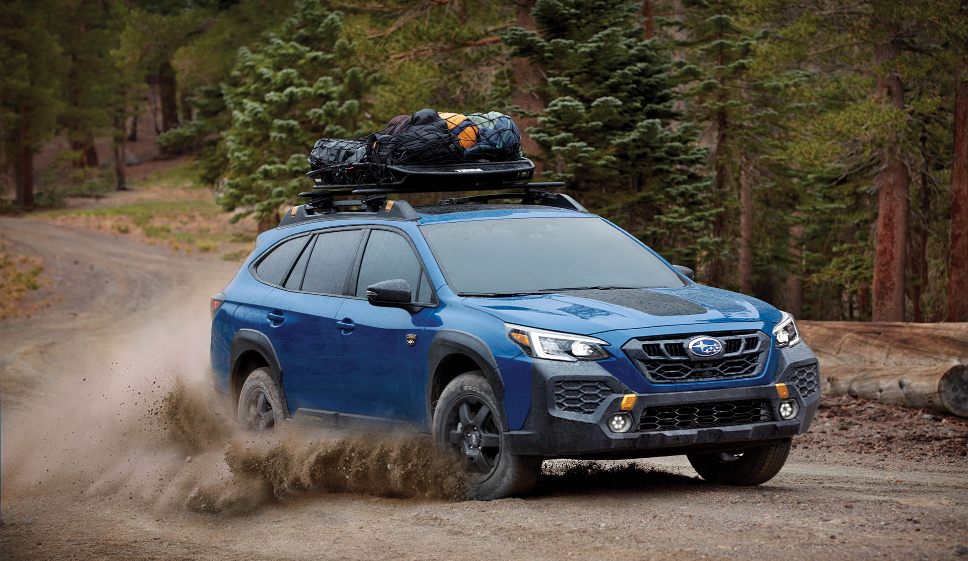 2025 Outback Wilderness driving on gravel road with cargo basket on the roof.