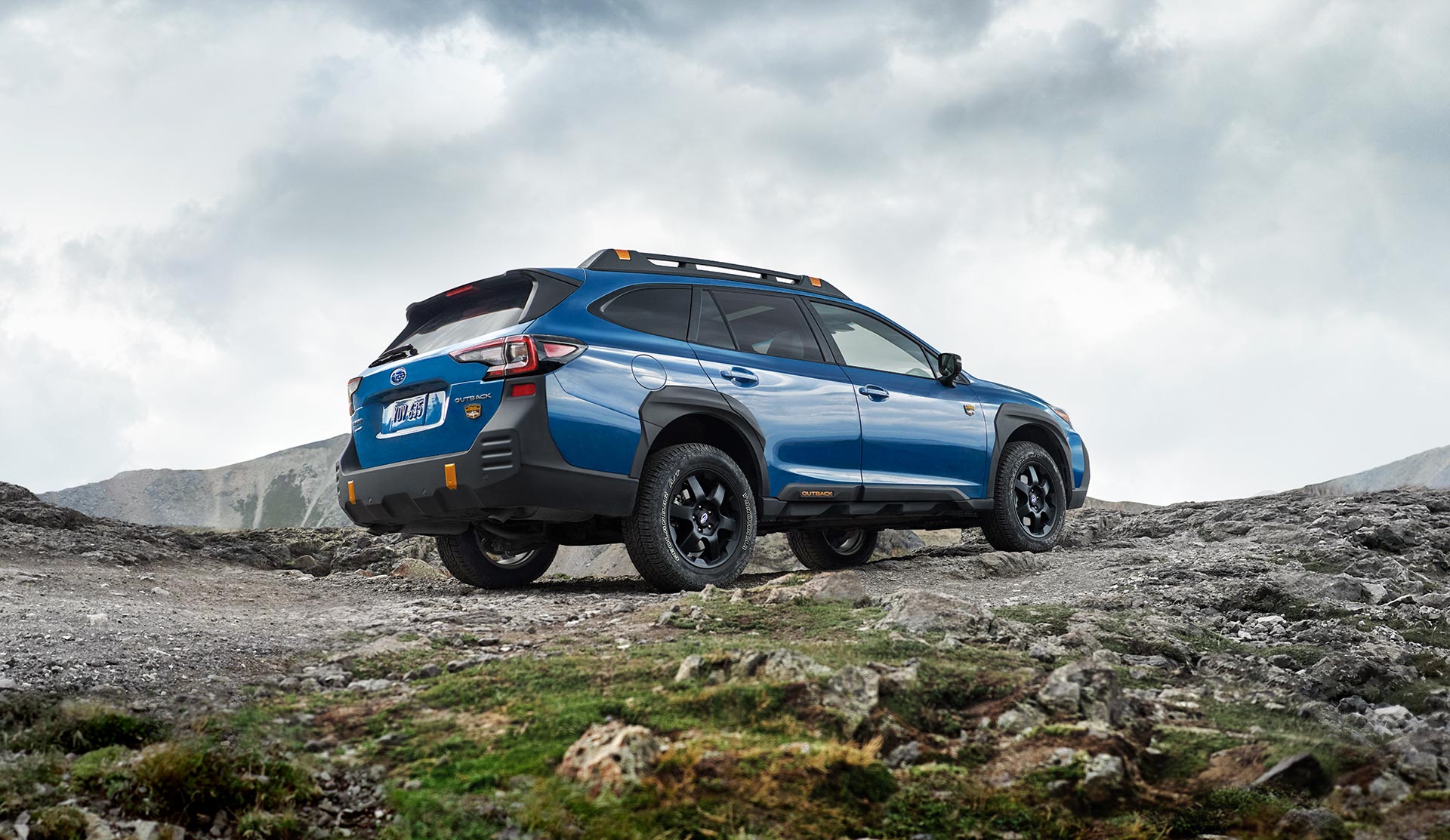 Rear shot of 2025 Outback Wilderness driving on rocky hilltop.